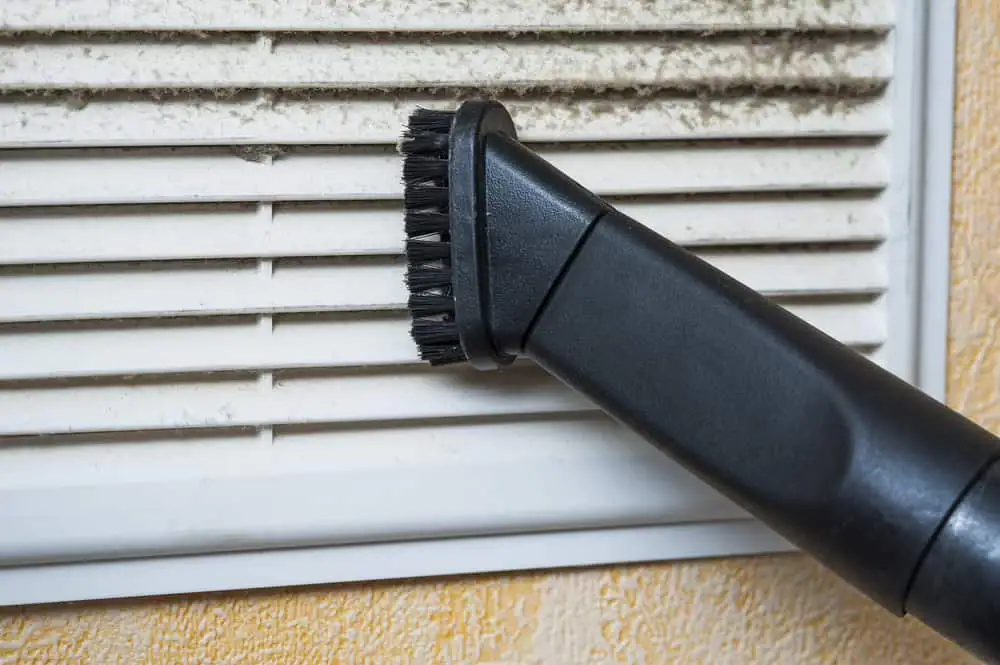 A vacuum cleaner brush attachment from a Central Vacuum System Long Island expertly cleans dust and dirt from the slats of a white air vent in NY.